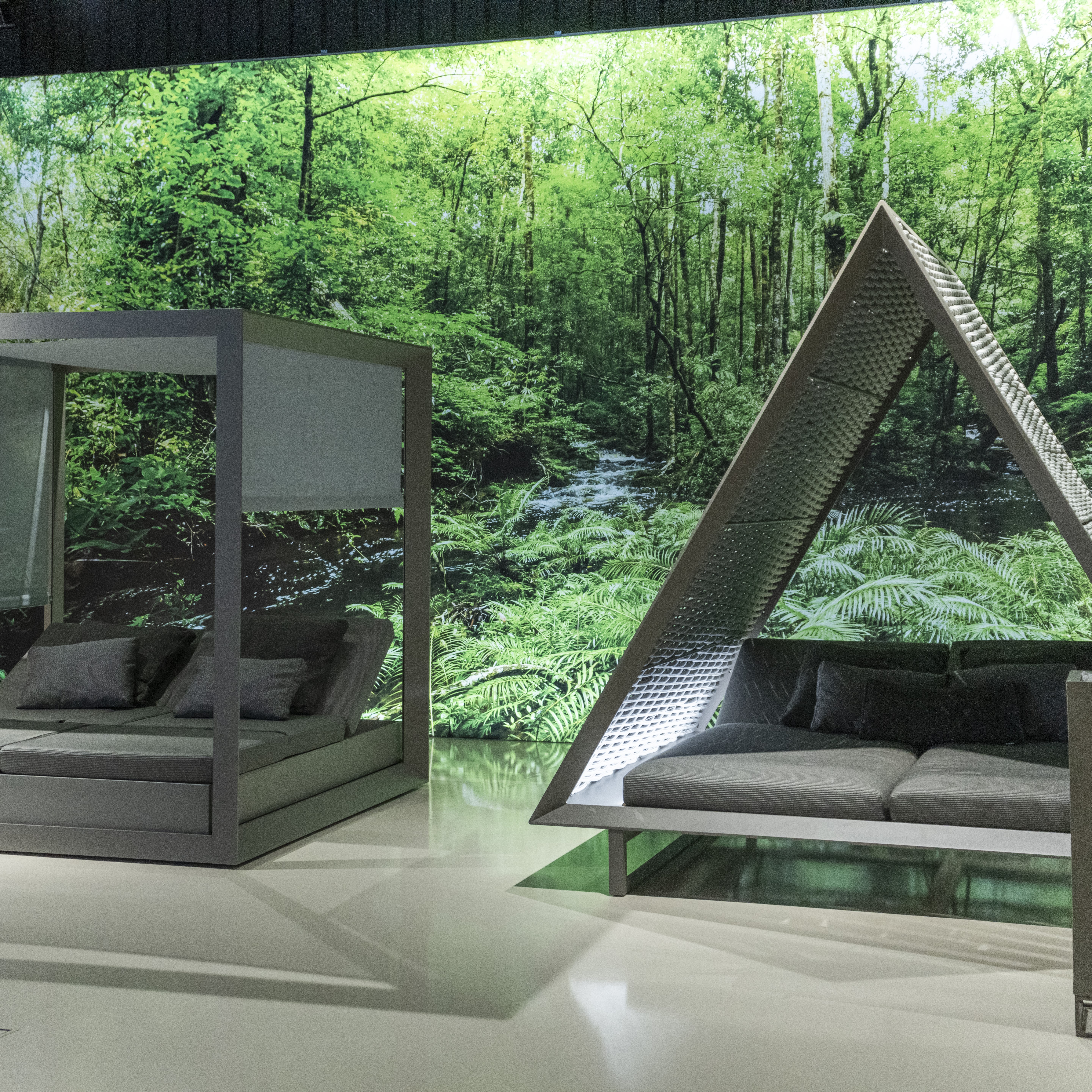 Caja de luz gigante en showroom Vondom con imagen de bosque y mobiliario de exterior bajo estructura triangular.