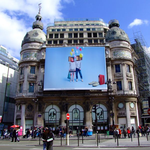 Lona publicitaria de gran formato instalada en la fachada de un edificio histórico. Diseño colorido con elementos modernos, ideal para captar atención en exteriores en áreas urbanas concurridas.