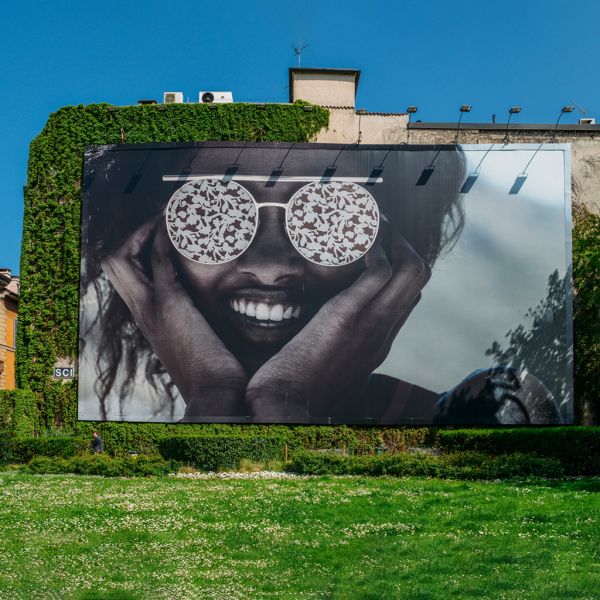 Lona publicitaria de gran formato instalada en la pared de un edificio, con diseño artístico de un rostro sonriente, ideal para espacios exteriores y campañas de impacto.